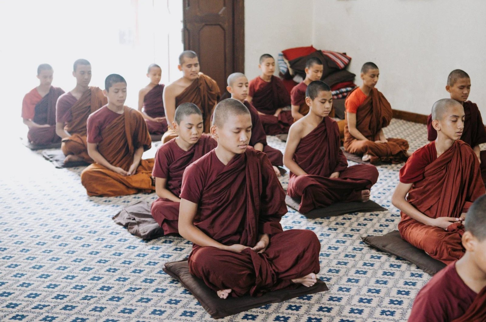Rows of young monks in maroon and saffron robes meditating on cushions