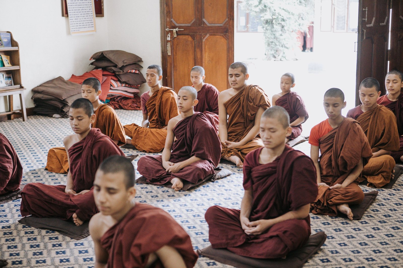 A wide view of young monks meditating across a sunlit hall