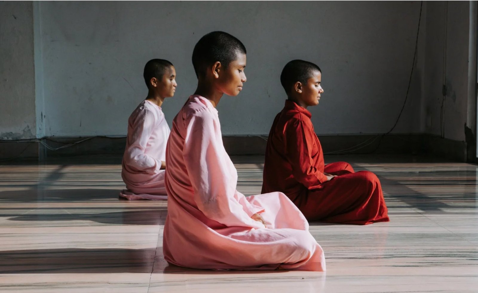 Three young nuns meditating in a shaft of sunlight on a polished floor