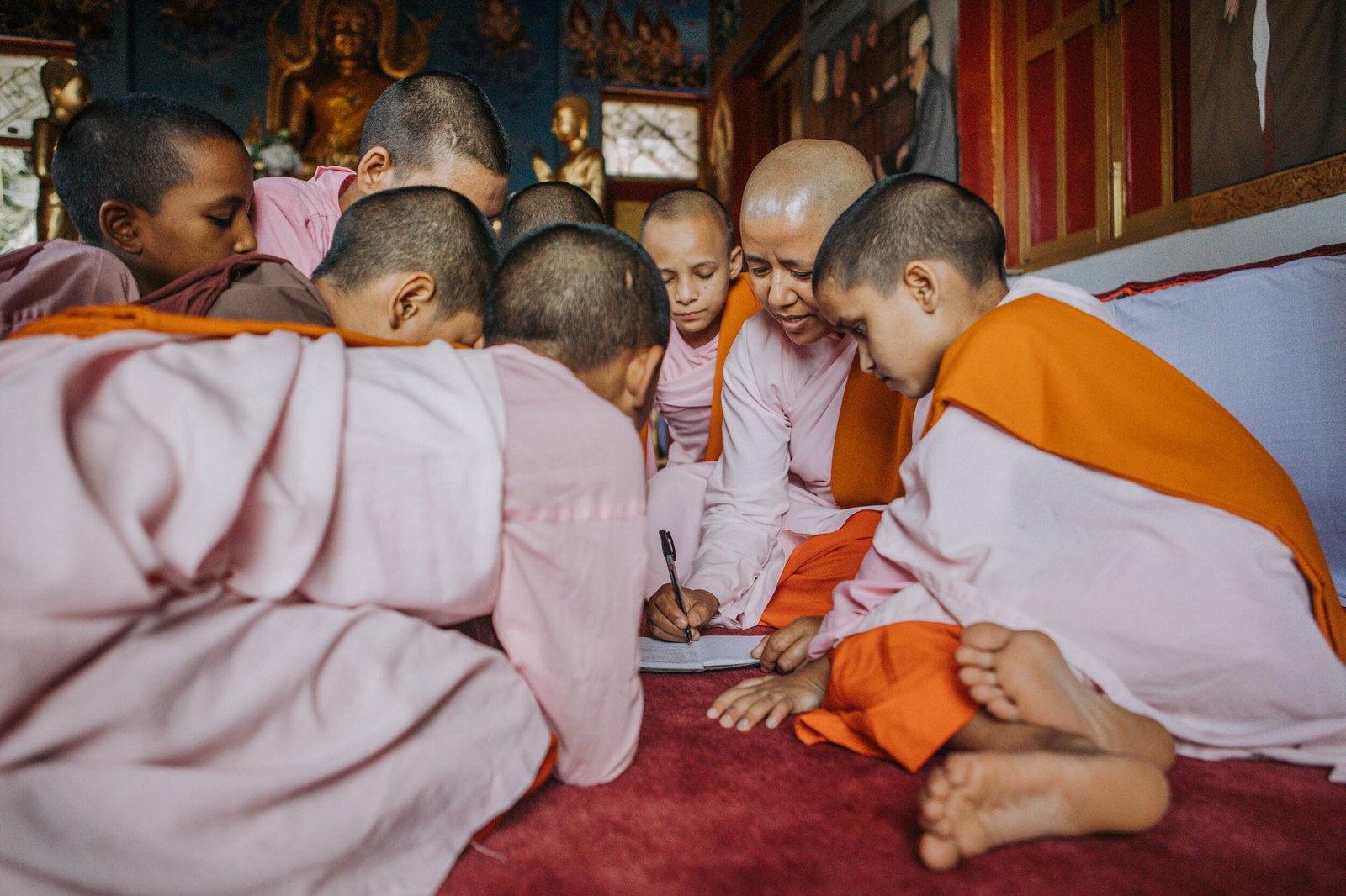 A nun teaching a circle of young novices gathered closely around an open notebook