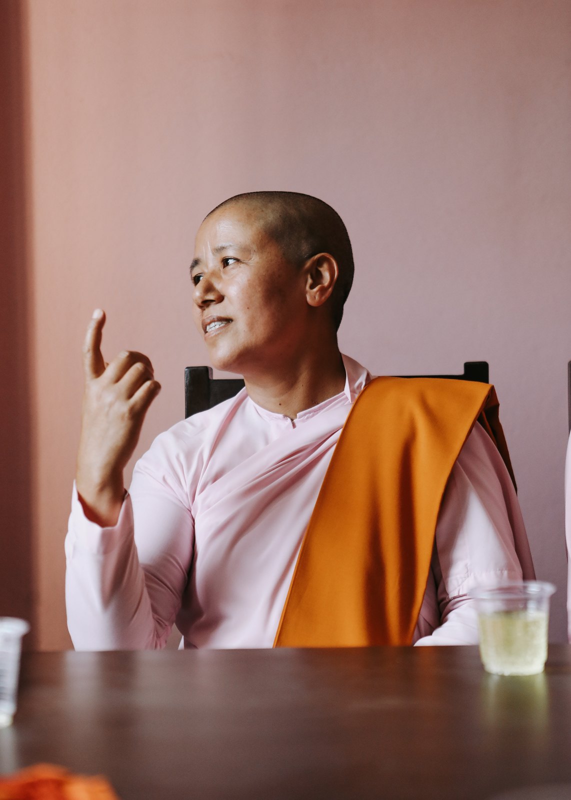 A nun in pink and saffron robes raising a finger mid-teaching
